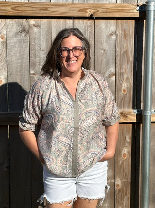 Person on a wooden deck wearing a patterned shirt and white shorts.