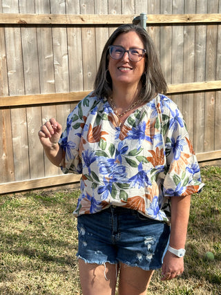 Person wearing a floral shirt and denim shorts on a wooden deck with grass in the background