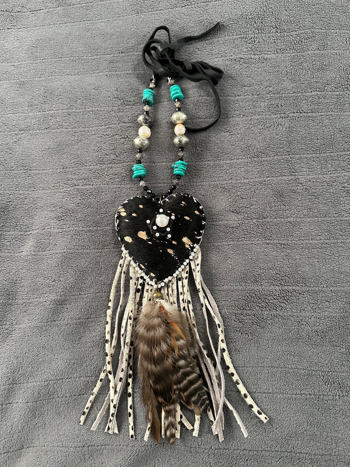 Heart-shaped decorative hanging with beads and feathers on a gray textured background