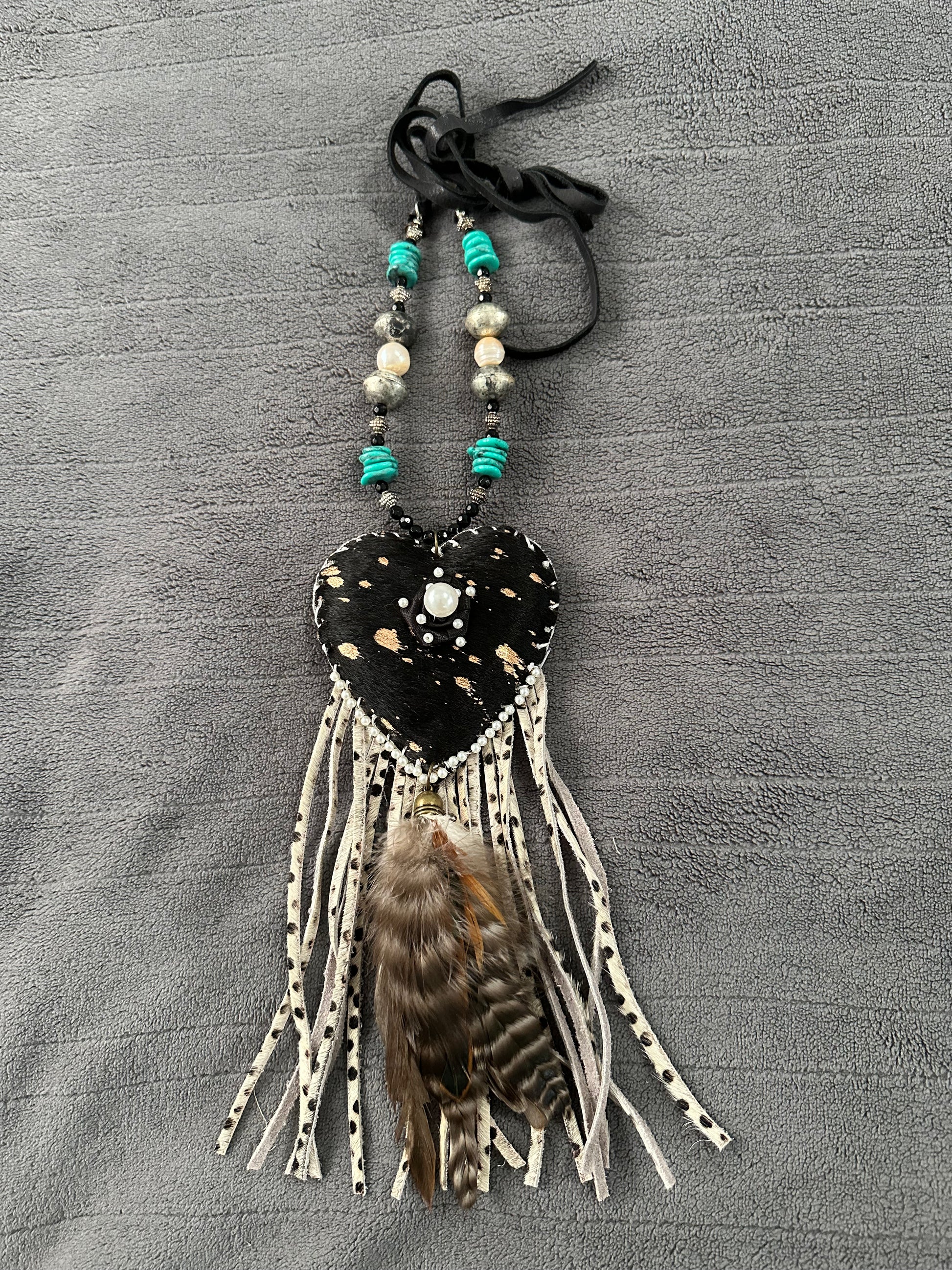 Heart-shaped decorative hanging with beads and feathers on a gray textured background